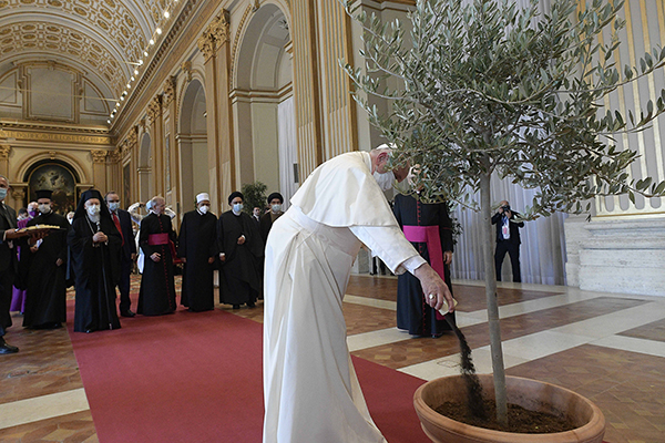Pope Francis pours dirt into a potted olive tree during the meeting, “Faith and Science: Towards COP26,” with religious leaders in the Hall of Benedictions at the Vatican Oct. 4, 2021. The meeting was part of the run-up to the U.N. Climate Change Conference, called COP26, in Glasgow, Scotland, Oct. 31 to Nov. 12, 2021. (CNS photo/Vatican Media)