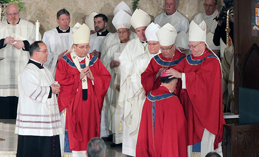On May 3, James F. Checchio was installed as the fifth bishop of Metuchen in an afternoon ceremony at Church of the Sacred Heart in South Plainfield. Bishop Dennis Sullivan, as co-consecrator, performs the laying-on-of-hands on Bishop Checchio during the Rite of episcopal ordination. Also on the altar are Archbishop John J. Myers of Newark, principal consecrator, and Bishop Paul Bootkoski, Bishop Emeritus of Metuchen and co-consecrator. Left, Bishop Checchio speaks with reporters during a post-ordination question-and-answer session.
Photo by Mike Walsh