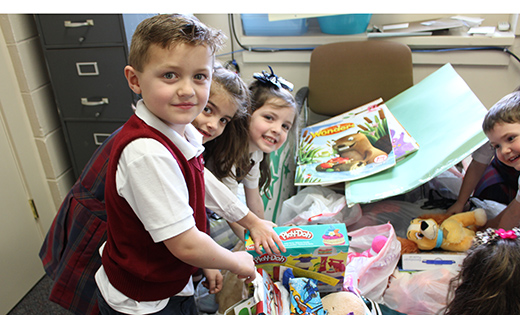 Kindergarten students Billy Cox, Maria DelQuadro and Mia Wrigley of Saint Michael Regional School, Clayton, collect items to donate to the Cradles to Crayons Organization for their monthly service project. Local children from birth to 12 years old, who are homeless or belong to low-income families, benefit from the new or nearly new items that are collected.
