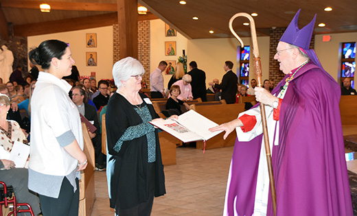 Kristen Ahern from Haddon Heights’ Saint Rose of Lime Parish stands in front of Bishop Dennis Sullivan with Betty Wells, the parish’s RCIA secretary.  Wells is presenting to Bishop the Book of Elect, signifying Ahern’s desire to enter the Catholic Church at the Easter Vigil.

Photo by James A. McBride