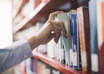 Woman at the library, she is searching books on the bookshelf and picking a textbook, hand close up