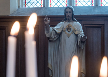 Statue of Jesus Christ in Church with Lit Burning Candles in Foreground