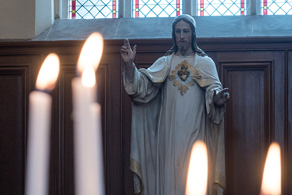 Statue of Jesus Christ in Church with Lit Burning Candles in Foreground