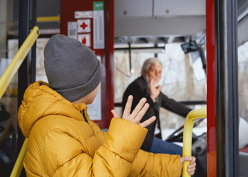 Back view of little boy in grey cap standing near open door saying goodbye to driver in transport. Crop of child male in orange jacket waving to driver getting off bus. Concept of politeness.