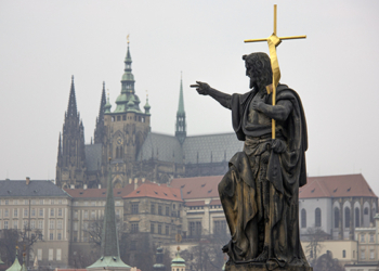 Sculpture of Saint John the Baptist bearing cross on Charles bridge with Prague Castle and  St. Vitus Cathedral in the background, Prague, Czech Republic