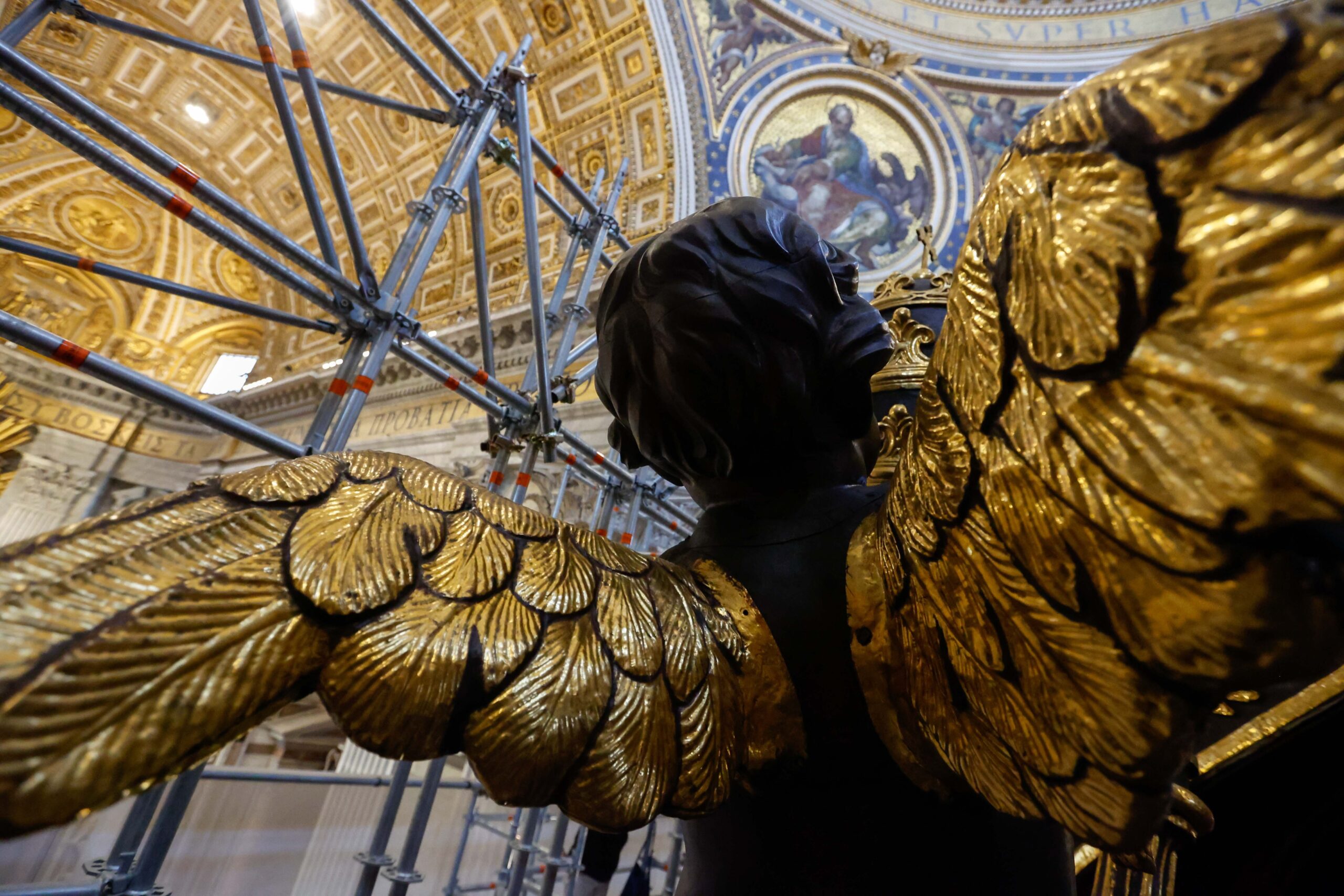 A statue of a cherub with gilded wings is seen against the backdrop of scaffolding and mosaics inside St. Peter’s Basilica during restoration work on the 17th-century canopy over the main altar at the Vatican Oct. 8, 2024. (CNS photo/Lola Gomez)