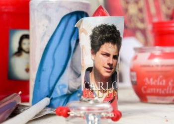 Votive candles and religious images, including one of Blessed Carlo Acutis, are seen at the base of a statue of St. John Paul II outside Rome's Gemelli hospital Feb. 27, 2025, while Pope Francis is being treated there for double pneumonia. (CNS photo/Lola Gomez)