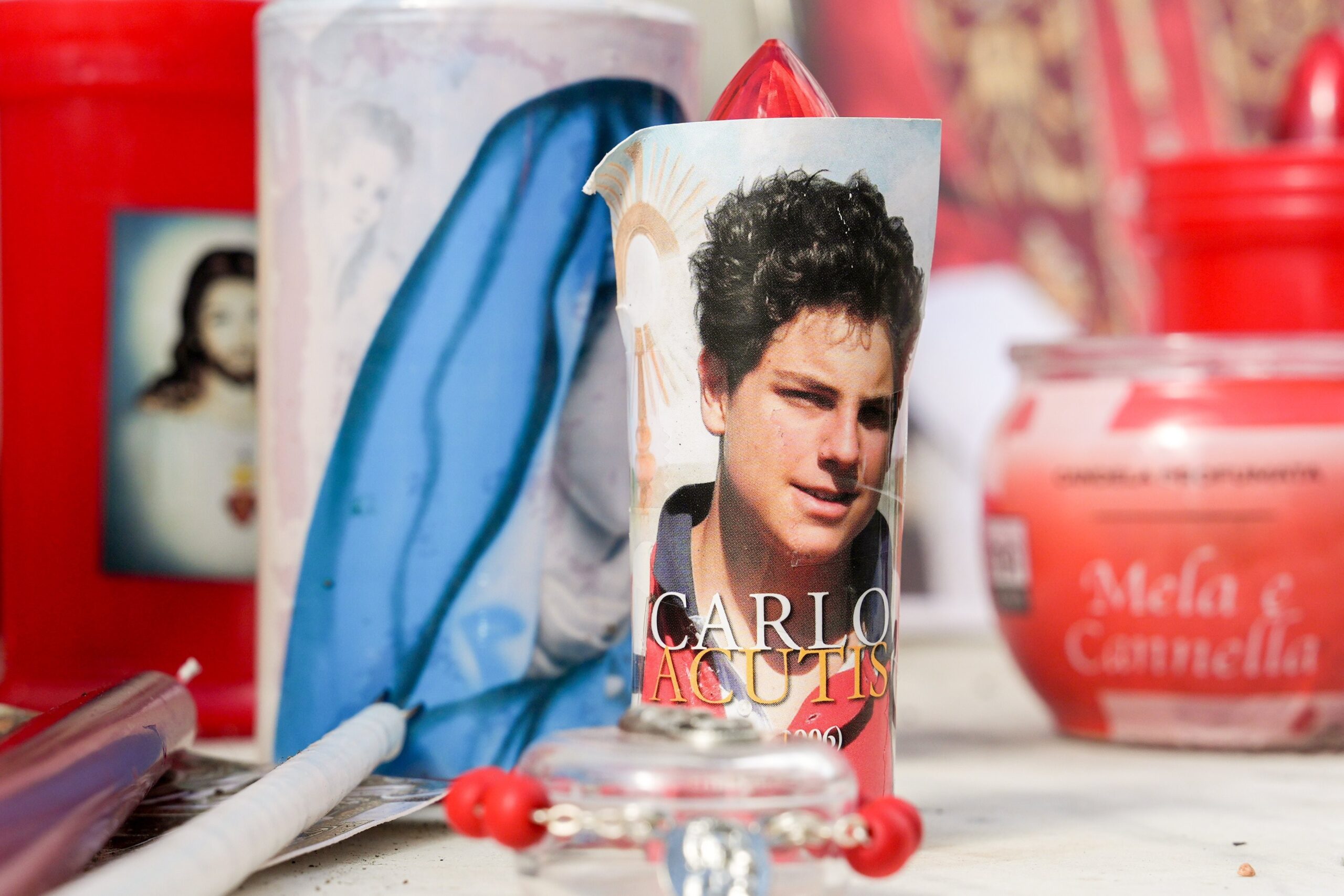 Votive candles and religious images, including one of Blessed Carlo Acutis, are seen at the base of a statue of St. John Paul II outside Rome's Gemelli hospital Feb. 27, 2025, while Pope Francis is being treated there for double pneumonia. (CNS photo/Lola Gomez)