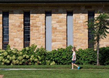 A child walks past boarded up windows outside the Annunciation Church in Minneapolis Aug. 28, 2025, which is a home to an elementary school and was the scene of a shooting the day before. A shooter opened fire with a rifle through the windows of the school's church and struck children attending Mass Aug. 27 during the first week of school, killing two and wounding 17 people in an act of violence the police chief called "absolutely incomprehensible."  (OSV News photo/Tim Evans, Reuters)