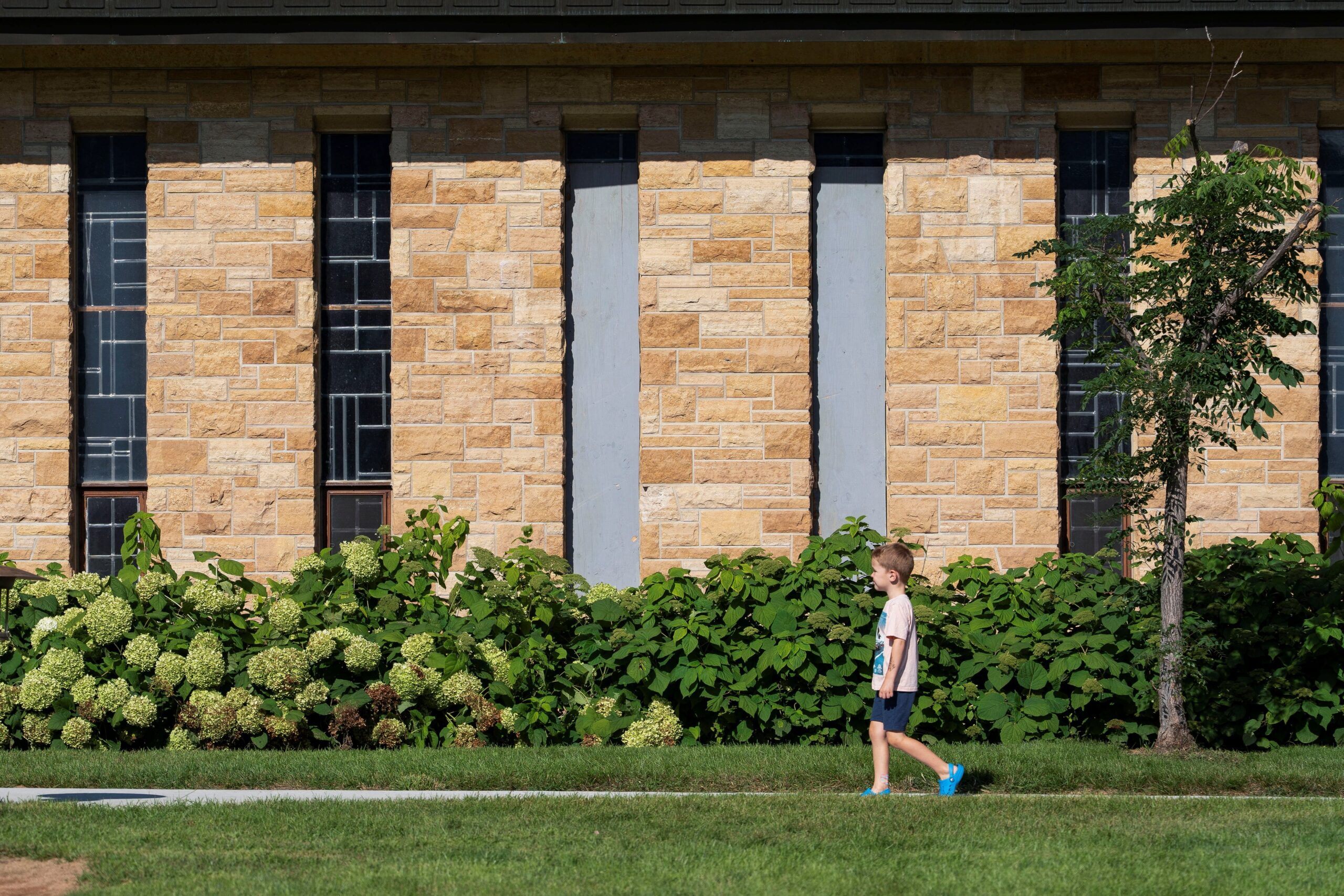 A child walks past boarded up windows outside the Annunciation Church in Minneapolis Aug. 28, 2025, which is a home to an elementary school and was the scene of a shooting the day before. A shooter opened fire with a rifle through the windows of the school's church and struck children attending Mass Aug. 27 during the first week of school, killing two and wounding 17 people in an act of violence the police chief called "absolutely incomprehensible."  (OSV News photo/Tim Evans, Reuters)