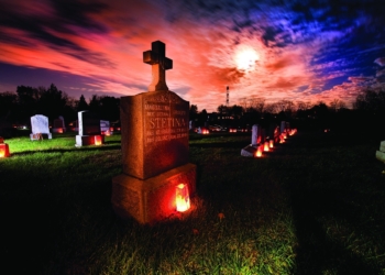 The grave marker of a couple is illuminated with a candle as a full moon shines through clouds in this undated file photo. Catholics pray for the dead during Mass, during designated days such as All Soul's Day, and often ask that Masses be celebrated for our loved ones during the anniversary of their death (OSV News photo/CNS/Lisa Johnston, St. Louis Review)