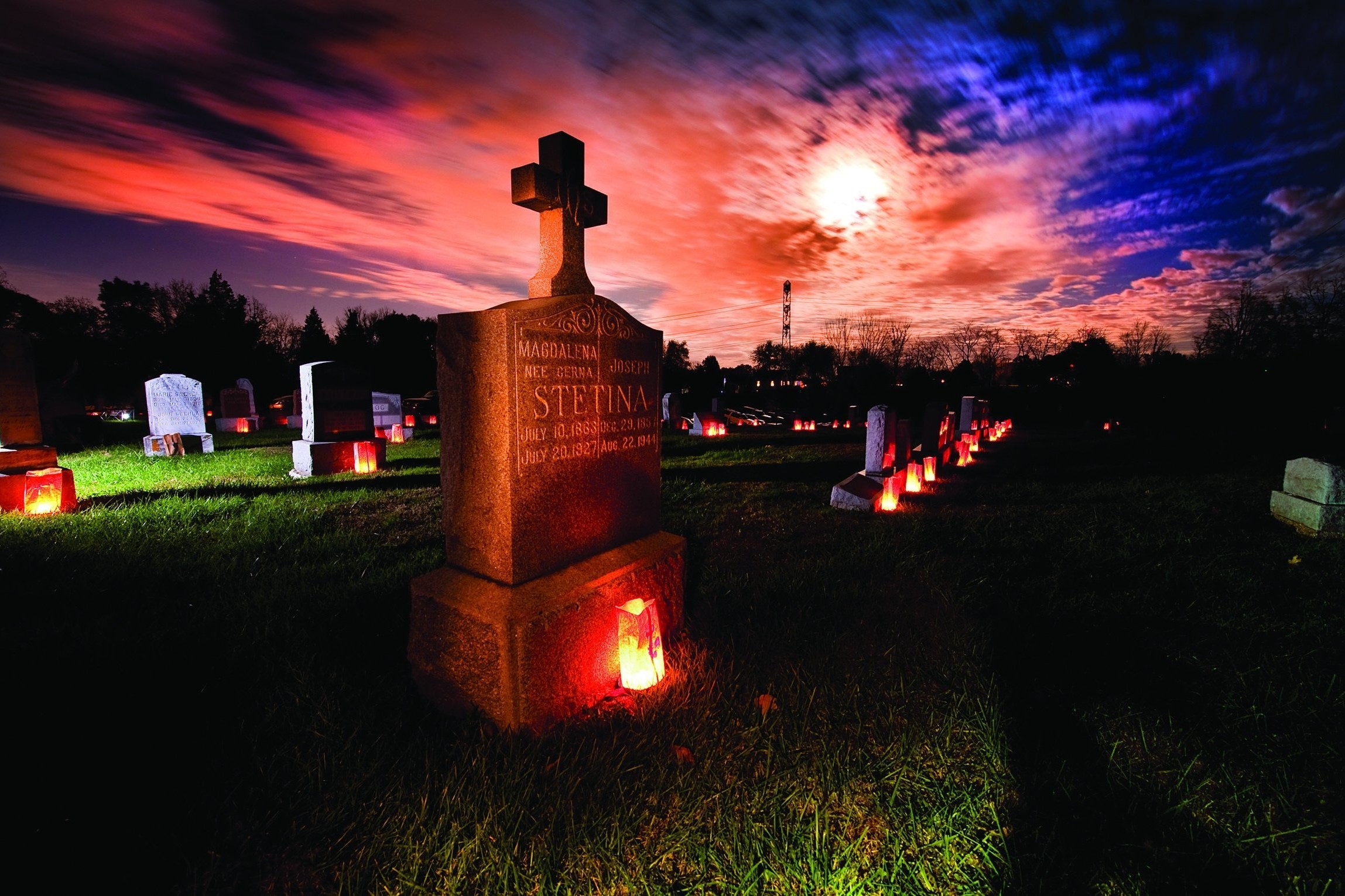 The grave marker of a couple is illuminated with a candle as a full moon shines through clouds in this undated file photo. Catholics pray for the dead during Mass, during designated days such as All Soul's Day, and often ask that Masses be celebrated for our loved ones during the anniversary of their death (OSV News photo/CNS/Lisa Johnston, St. Louis Review)