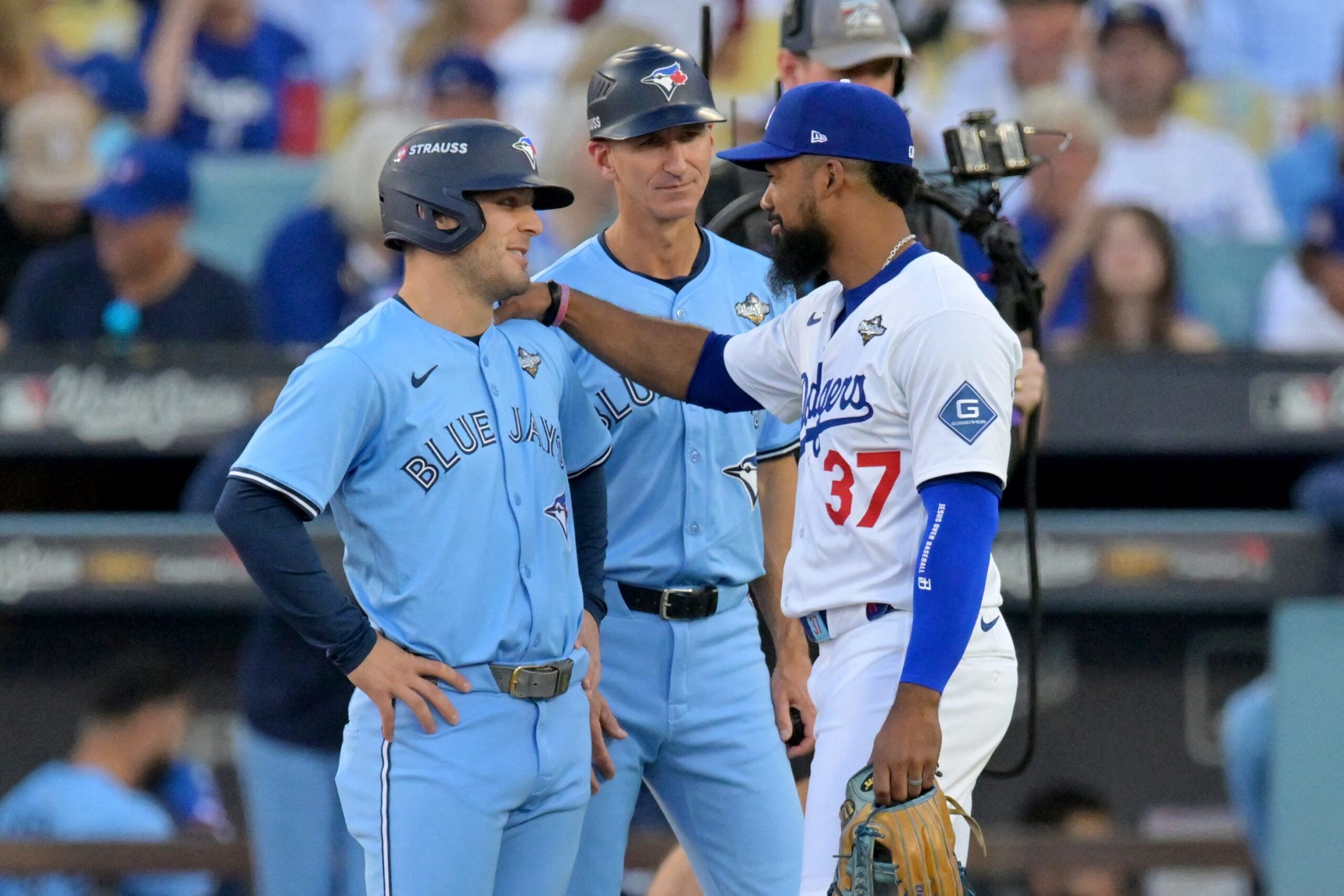 Los Angeles Dodgers right fielder Teoscar Hernandez (37) and Toronto Blue Jays center fielder Daulton Varsho (5) talk as first base coach Mark Budzinski (53) looks on during a challenge on a play in the first inning during game five of the 2025 MLB World Series at Dodger Stadium in Los Angeles Oct. 29, 2025. Mandatory Credit: (OSV News photo/Jayne Kamin-Oncea-Imagn Images via Reuters)