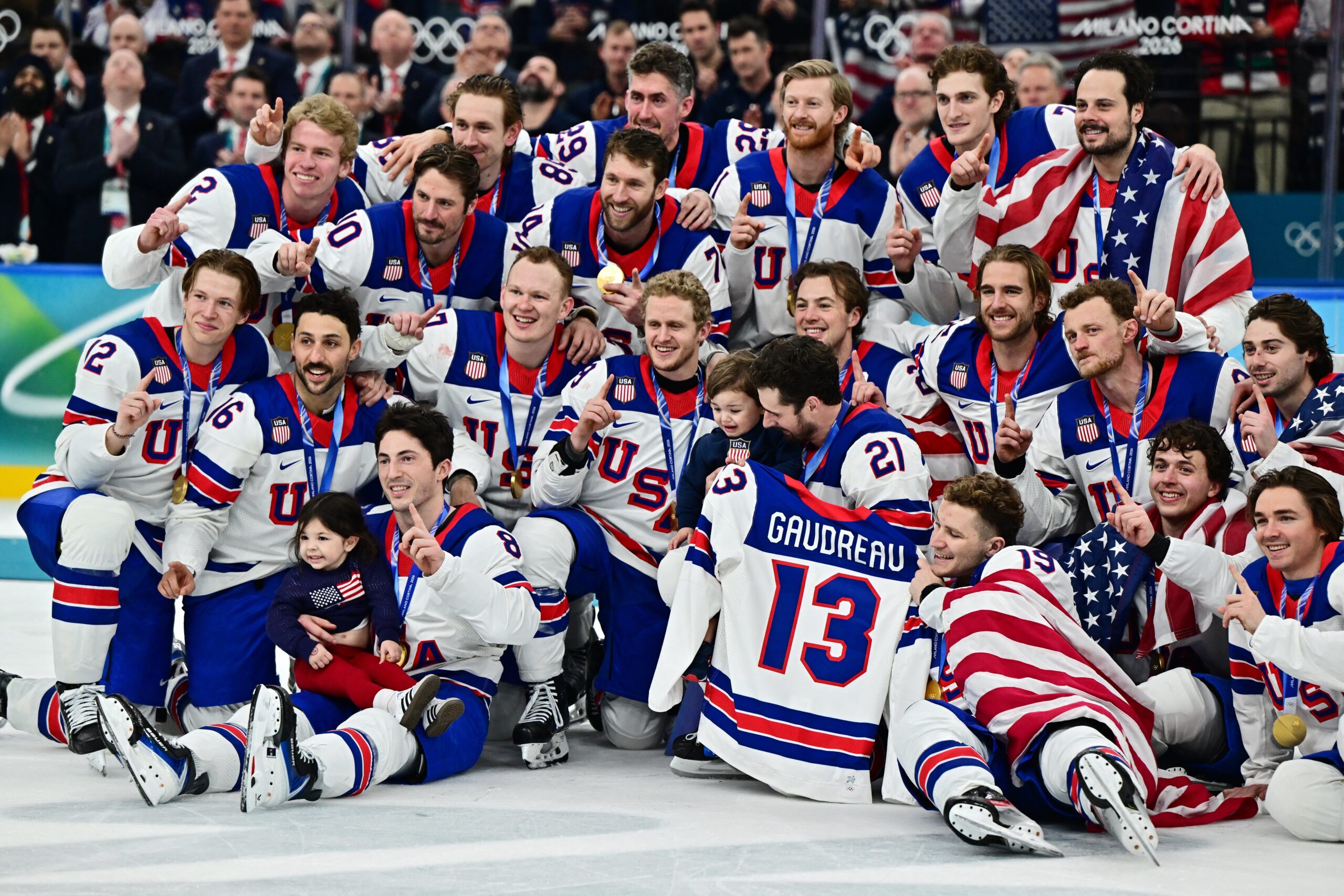 Gold medalists of the U.S. men's hockey team hold up the jersey of the late John Gaudreau and celebrate with his children Noa Harper Gaudreau and Johnny Edward Gaudreau as they pose for a photograph as they celebrate with their medals during the ceremony after defeating Canada 2-1 in overtime during the Milano Cortina 2026 Olympics at Milano Santagiulia Ice Hockey Arena in Milan, Italy, Feb. 22. Gaudreau, and his brother Matthew, who were Catholic, were killed the evening of Aug. 30, 2024, when they were struck by Sean M. Higgins of Woodstown, N.J., a suspected drunk driver, while bicycling in Oldmans Township, close to their hometown in Salem County, N.J. (OSV News photo/Marton Monus, Reuters)